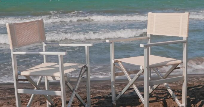 Two empty beach chairs in front of the beach with the rough sea