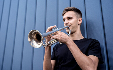 Young street musician playing the trumpet near the big blue wall