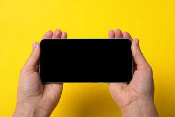 Smartphone in female hands with black screen over yellow background