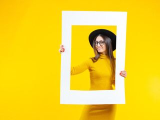 Beautiful woman holds a frame and smiles - isolated over yellow. ?heerful girl in the picture....