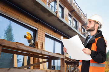 A man with drawings next to a house under construction. The project of a wooden cottage. Turnkey...