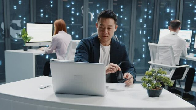 Chinese handsome executive wearing headset microphone and using computer laptop at data center. Server room customer support. Operator. Telecommunications.