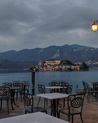 tables in the outdoor area of the main square of Orta San Giulio with the island of San Giulio in the background at dawn