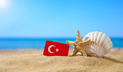 Fototapeta na wymiar Tropical beach with seashells and Turkey flag. The concept of a paradise vacation on the beaches of Turkey.