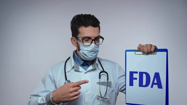 Young bearded doctor with stethoscope showes paper holder with FDA abbreviation on isolated white background