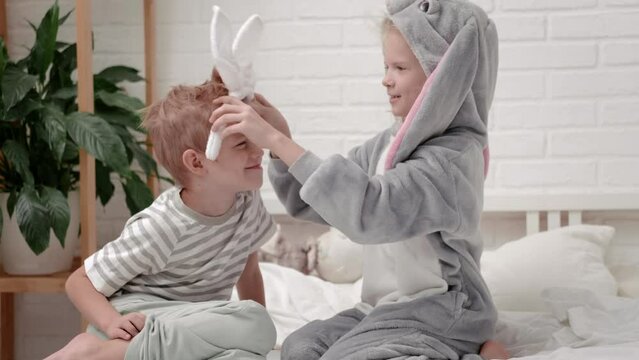 Girl in rabbit costume bunny ears on head jumping on white bed Excited caucasian child having fun at home enjoy laughing playing funny active game in bedroom,Happy Easter celebration.