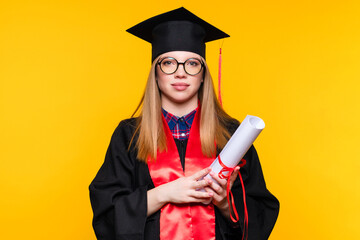 Girl graduate in graduation hat and eyewear with diploma on yellow background. Blonde young woman...