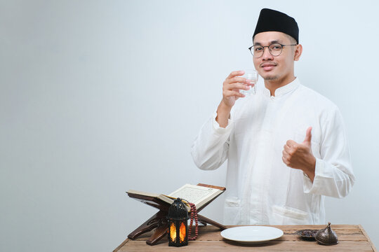 Asian muslim man smiling and thumbs up while going to drink a glass of water for break fasting
