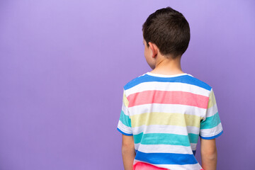 Little boy isolated on purple background in back position and looking side
