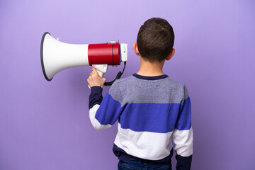 Little boy isolated on purple background holding a megaphone and in back position