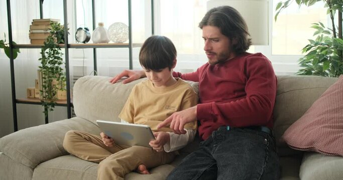 Father cheering for son playing on digital tablet at home