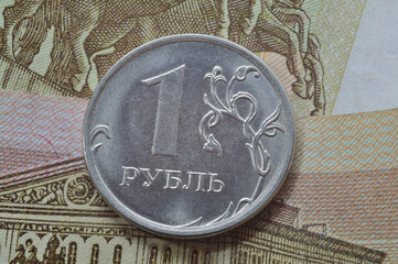 Russian coin with a face value of 1 ruble lies on a banknote. Translation of the inscriptions on the coin: "1 ruble"