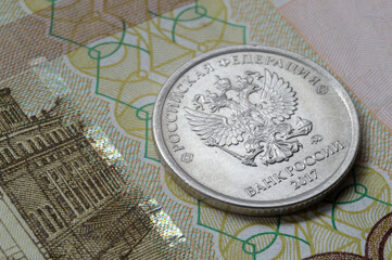 Russian coin with a face value of 1 ruble lies on a banknote. Translation of the inscriptions on the coin: "Russian Federation, Bank of Russia"