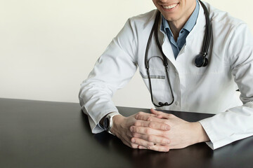 Close-up of a male doctor or general practitioner in a white medical uniform with a stethoscope shows quality medical care. A doctor with a phonendoscope sits at table 