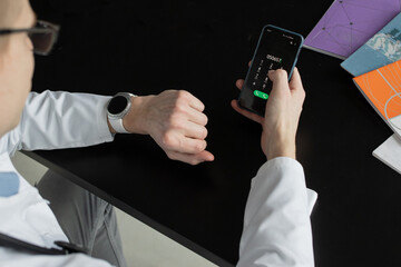 Close-up of a male doctor or general practitioner in a white medical uniform with a stethoscope and a phone in his hand demonstrates quality medical care. Doctor with phonendoscope and smartphone