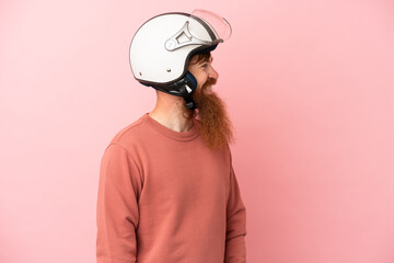 Young reddish caucasian man with a motorcycle helmet isolated on pink background looking side
