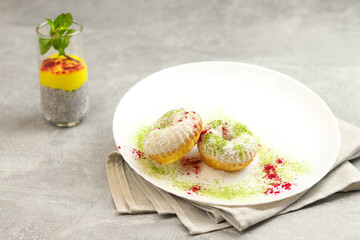 Vegan donuts topped with healthy white glaze with coconut flakes and desiccated coconut on plate on gray background.