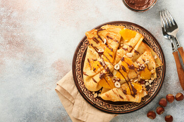 Crepes suzette with oranges and chocolate. Thin crepes with chocolate spread, hazelnuts and orange slices fruit in plate for breakfast on old concrete rustic table background. Copy space. Top view