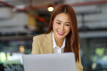 Attractive Asian businesswoman sitting working on laptop in office, smile and happily.