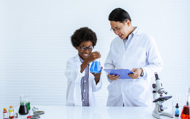 Asian male teacher is teaching science and experiment to African black boy in classroom at school....