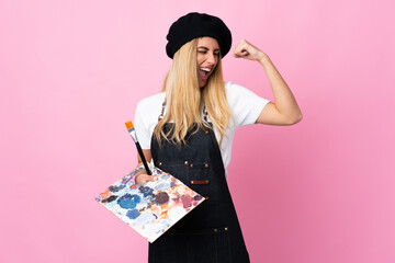 Young artist woman holding a palette over isolated pink background celebrating a victory