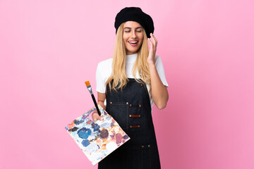 Young artist woman holding a palette over isolated pink background laughing