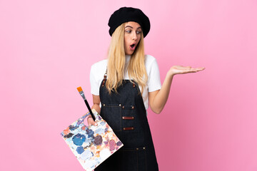 Young artist woman holding a palette over isolated pink background holding copyspace imaginary on the palm