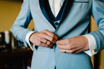 Man fastens the buttons. The groom in a suit, shirt standing in room. Close up.