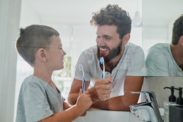 Got to take care of our teeth. Shot of a father and his little son brushing their teeth together in...