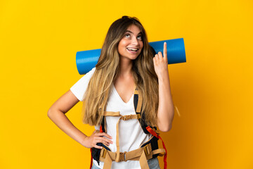 Young mountaineer woman with a big backpack isolated on yellow background thinking an idea pointing the finger up