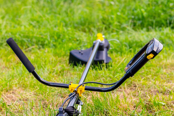 Fototapeta na wymiar Trimmer for mowing the grass in the garden among the thick grass