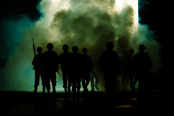 Obraz na płótnie Canvas silhouette group of thai soldiers special forces full team in uniform walking action through smoke and holding gun on hand and over the lighting background.