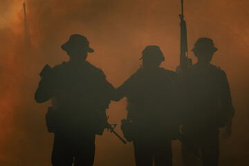 silhouette group of thai soldiers special forces full team in uniform walking action through smoke and holding gun on hand and over the lighting background.