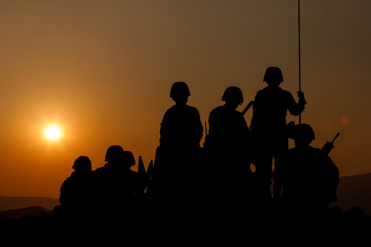 silhouette group of special forces sodiers standing and sit on tank with over the sunset background,