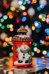 Christmas lantern with a snowman figurine against the background of multi-colored Christmas tree lights. Christmas decorations. bokeh. Christmas and New Year