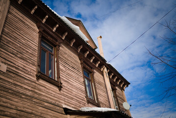 Rural wooden house with carved architraves and a carved roof. A sunny spring day, drops of water dripping from the roof from melting snow.