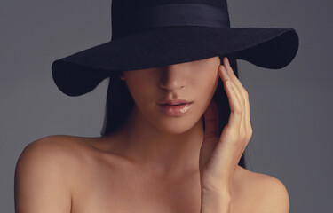 Shes a mystery. Studio shot of a beautiful woman wearing a hat against a gray background.