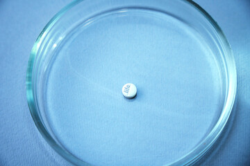 A male hand holds a glass plate with white pill inside. Petri dish for biological research.Isolated on background. Laboratory tests and research. Chemistry science or medical biology experiment 