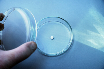 A male hand holds a glass plate with white pill inside. Petri dish for biological research.Isolated on background. Laboratory tests and research. Chemistry science or medical biology experiment 