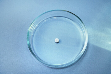 A male hand holds a glass plate with white pill inside. Petri dish for biological research.Isolated on background. Laboratory tests and research. Chemistry science or medical biology experiment 