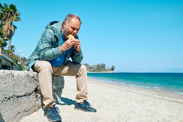 Bearded mature man at spring seaside eating hot palatable panzarotto (calzone pizza fried in hot oil). Typical Sicilian street food.