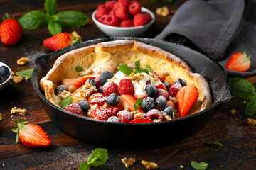 Dutch baby pancake with berries and icing sugar in a iron cast pan. Morning breakfast