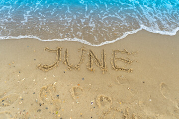 The word June is written on the sand of a beach by the sea. Washed off by a wave. The inscription disappears. End of summer concept. Back to school - Powered by Adobe