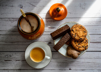 A cup of coffee, chocolate and oatmeal cookies, gingerbread, a pot of sugar on a wooden table
