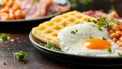 Potato waffles with fried egg, bacon and baked beans. Morning breakfast