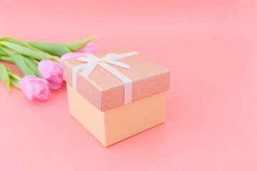 A box with a ribbon and beautiful pink tulips in a delicate magenta color on a pink background. Concept holiday, mother's day, birth, father's day, valentine's day, christmas. copyspace