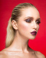 Fototapeta premium Portrait of young female model with makeup with bare shoulders, isolated on a red background. Beauty portrait.