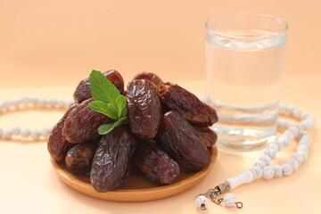 Date fruits in wooden plate, glass of water and white prayer beads. Fresh date fruits for iftar. Ramadan concept idea photo.