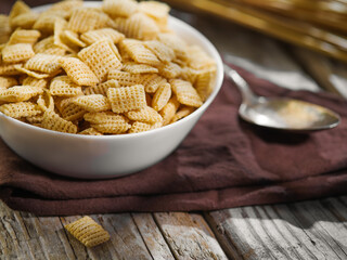 Close-up. On a brown napkin, a bowl with whole grain pads and a spoon. Wooden background. Quick grain breakfasts, children's, school, diet food. Organic food. Advertising, banner.