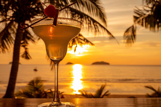 Cocktail glass decorated with a slice of lime and cherry on the background of the sea and sunset. Margarita cocktail.
